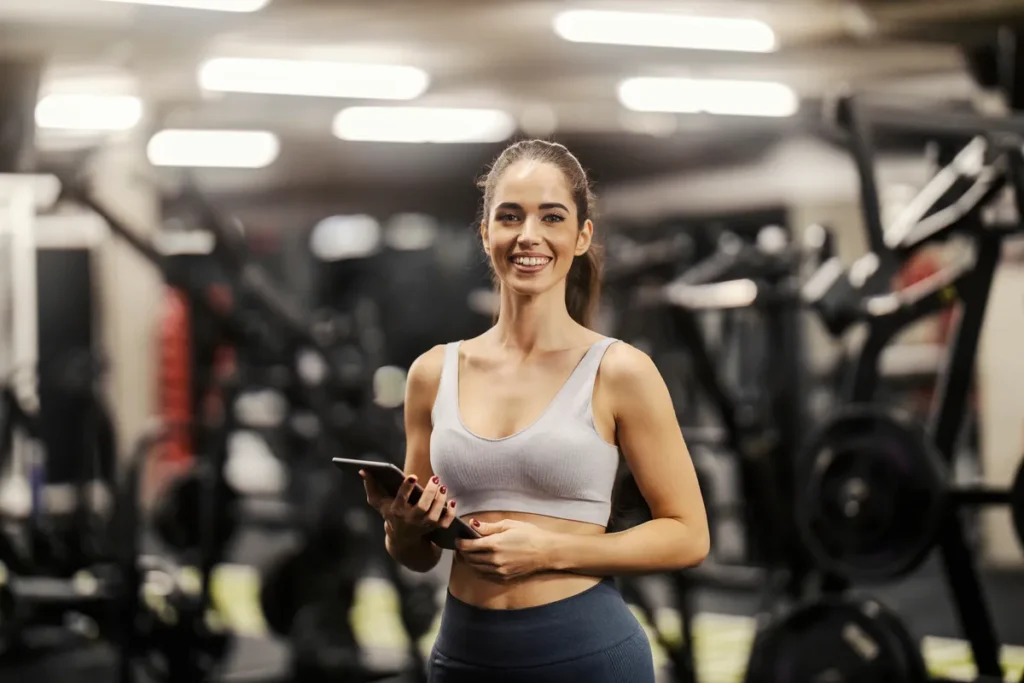 Gym owner smiling, holding a phone, in her fitness centre